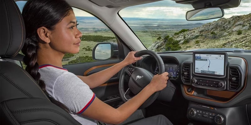 A woman with a braided ponytail driving a car with a navigation system visible, showing a map.