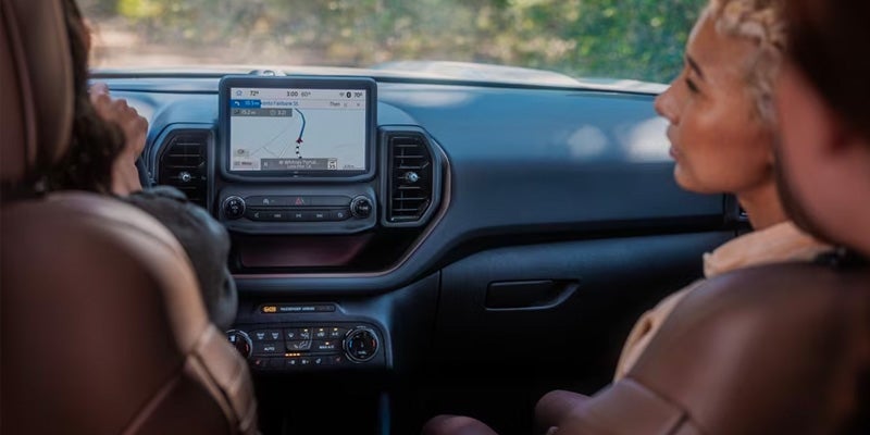 Inside a car, a navigator is on a center display, with a passenger at right and a driver obscured at left.