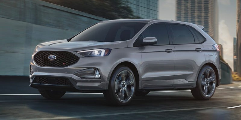 A modern gray Ford Edge ST SUV driving on a city road with blurred buildings in the background.