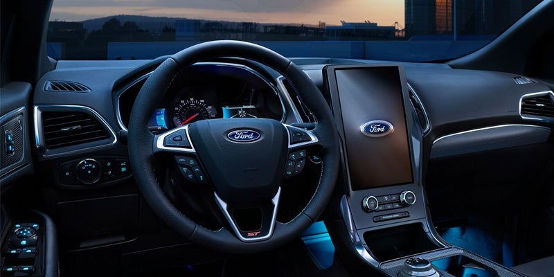 Interior shot of a dark car showing the dashboard, steering wheel with a Ford logo, and large vertical screen.