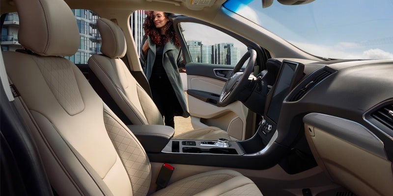 Interior of a car with beige seats, and a woman with curly hair getting into the driver's side door.