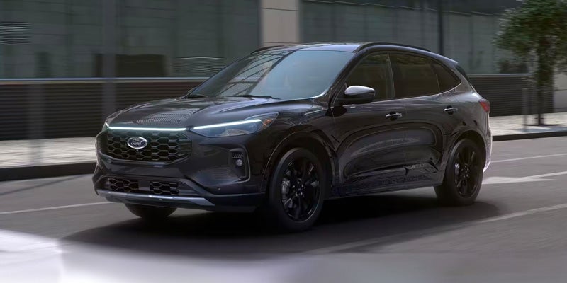 A charcoal gray Ford Escape SUV with a bright LED light strip above the grille drives on a city street.