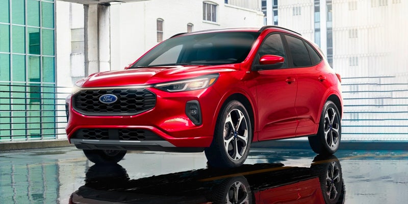 Front 3/4 view of a shiny red Ford Escape SUV with black grille, parked on a wet surface reflecting the vehicle.