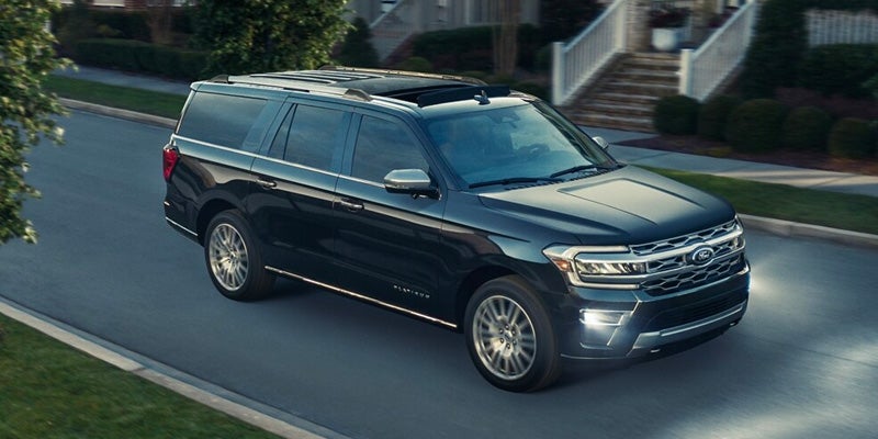 Dark blue Ford Expedition SUV driving along a suburban street with houses and trees in the background.