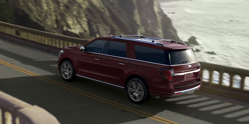 Maroon Ford Expedition SUV driving along a coastal highway with a cliff face on the left and ocean on the right.
