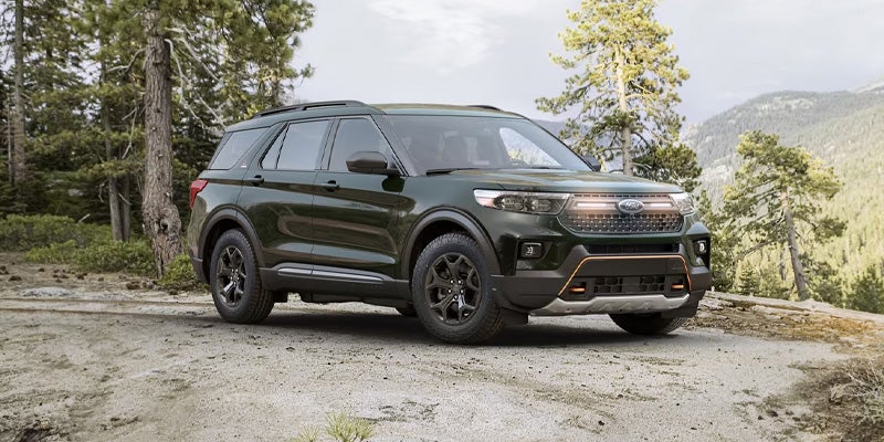 Dark green Ford Explorer SUV parked on a clearing, surrounded by pine trees and mountains in the distance.