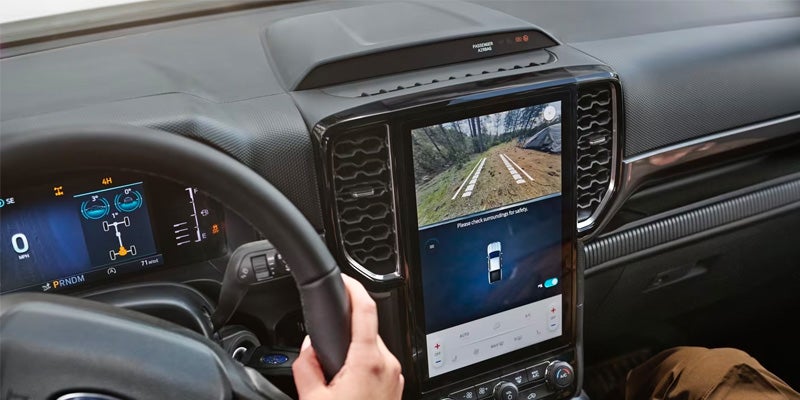 A driver's view of a car's dashboard with a large touchscreen showing an off-road backup camera view.