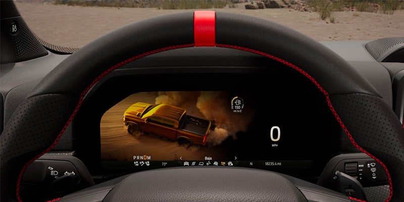 Close-up of a truck's steering wheel and digital gauge cluster showing a pickup truck driving off-road.