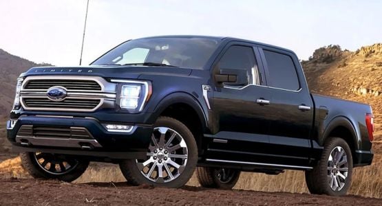 A dark blue Ford F-150 Limited pickup truck with chrome accents sits on a dirt road in front of hills.
