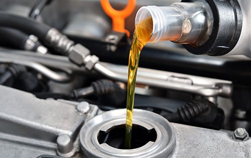 Golden motor oil pouring from a plastic bottle into an engine's oil fill cap.