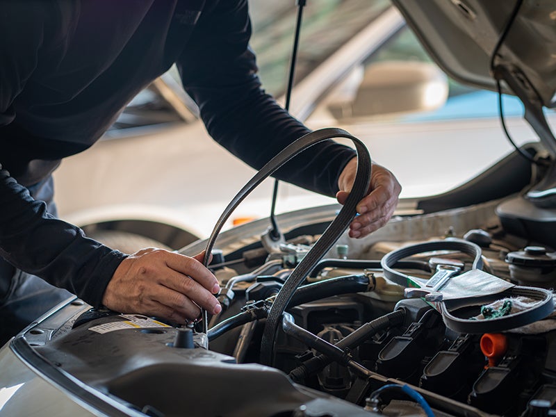 Mechanic with dirty hands replacing a serpentine belt on an engine with the hood open.